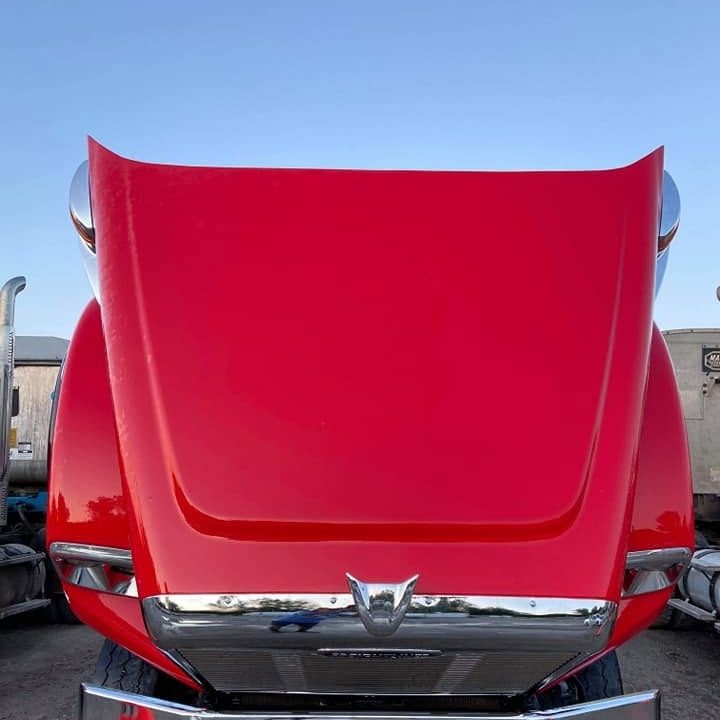 Front of a red truck with the hood raised and a glossy deep red finish, chrome bumper below.