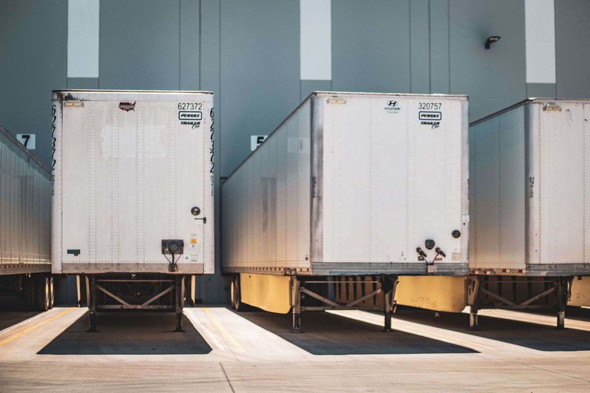 Three white dry van trailers backed into loading dock bays at a gray warehouse wall.