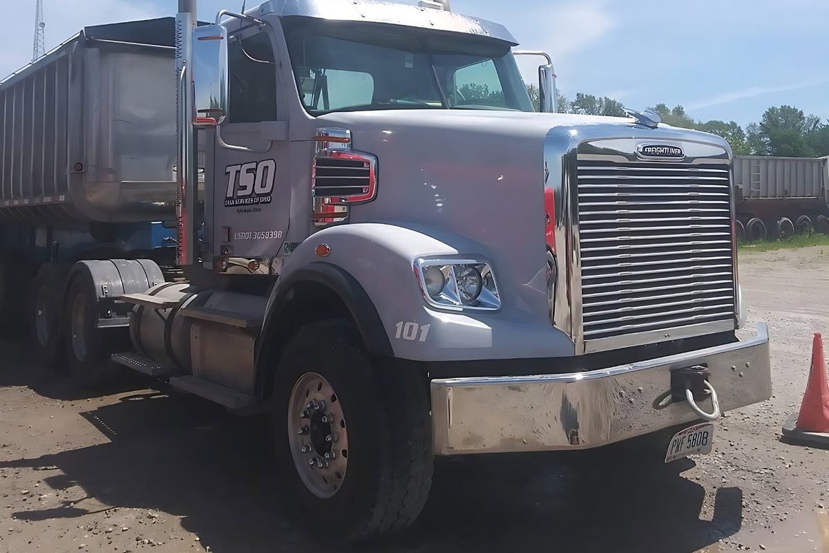 Silver dump-truck tractor with a chrome stack and mirror and an aluminum dump trailer behind it, under a blue sky.