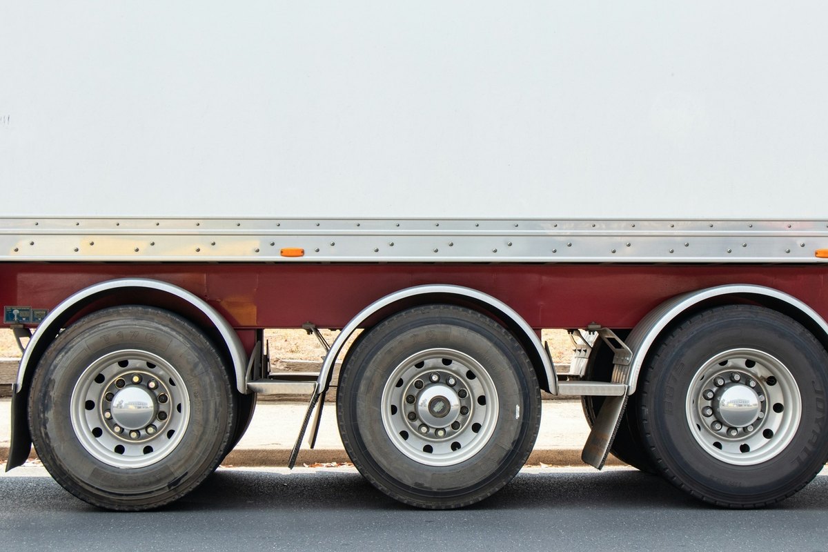 Aluminum rail strip and chrome hub caps on three tandem axles of a white trailer box.