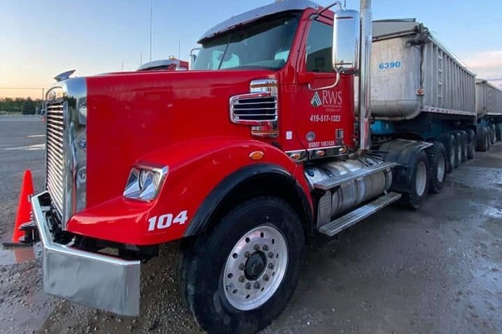 Dump-truck tractor cab in red with a mirror and stack, set against a dusk sky.