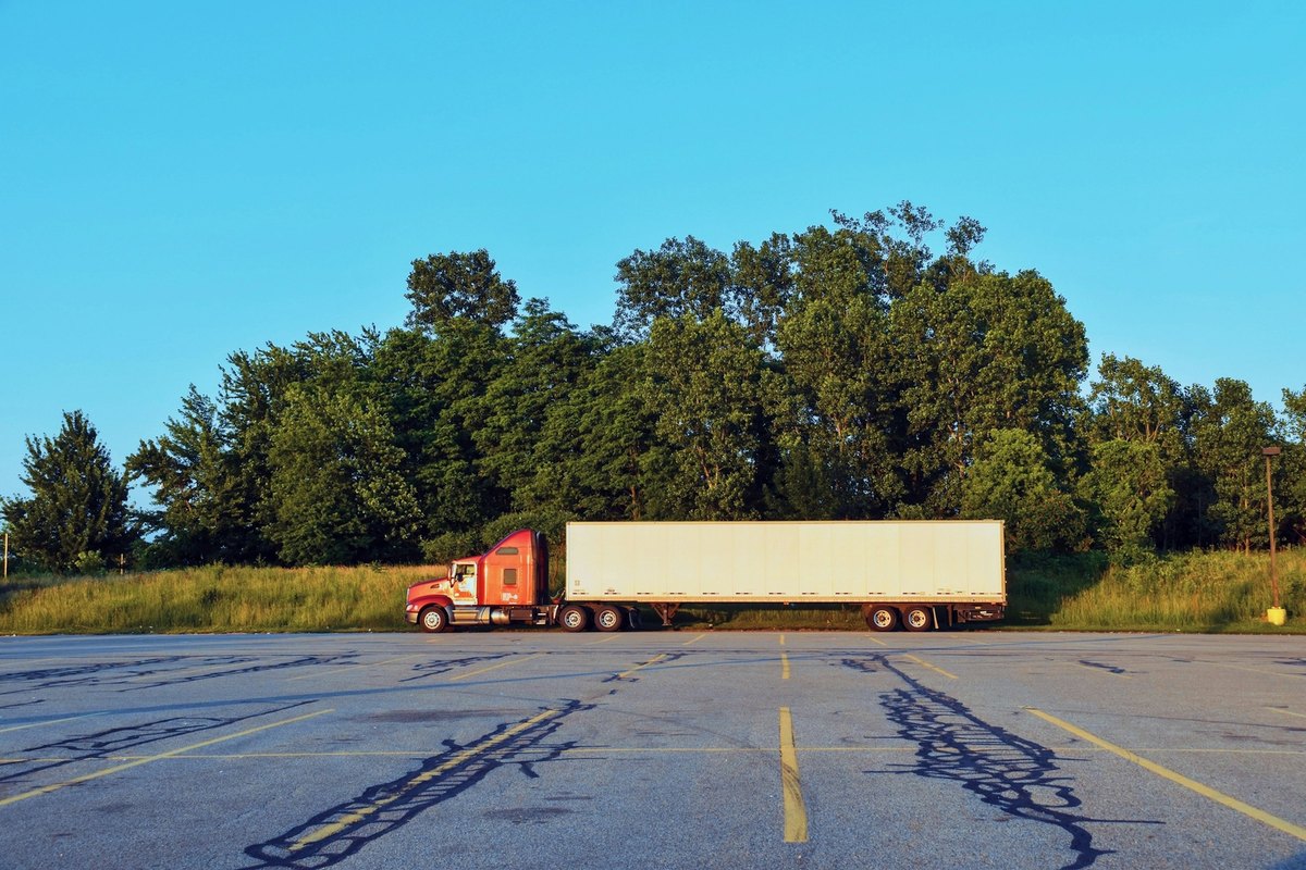 White 53-foot dry van trailer with a red tractor parked sideways in an empty lot beside a wall of trees.