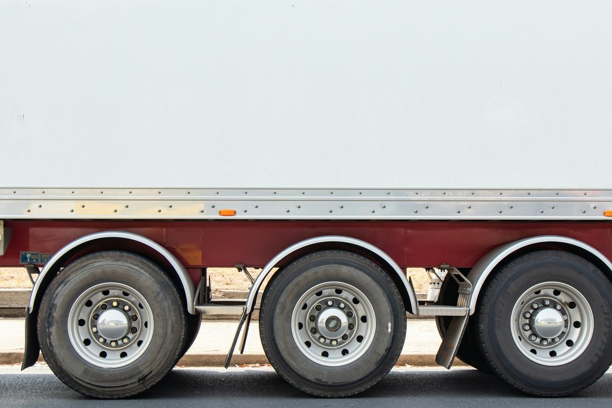 Three chrome hub caps and silver wheels on a white trailer box with a polished aluminum rail strip.