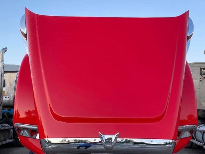 Red truck hood raised with a glossy deep red finish and polished chrome bumper.