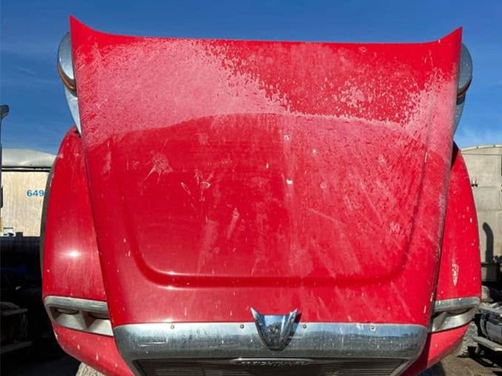 Red truck hood raised with the paint dulled by a film of dried road spray and spots.