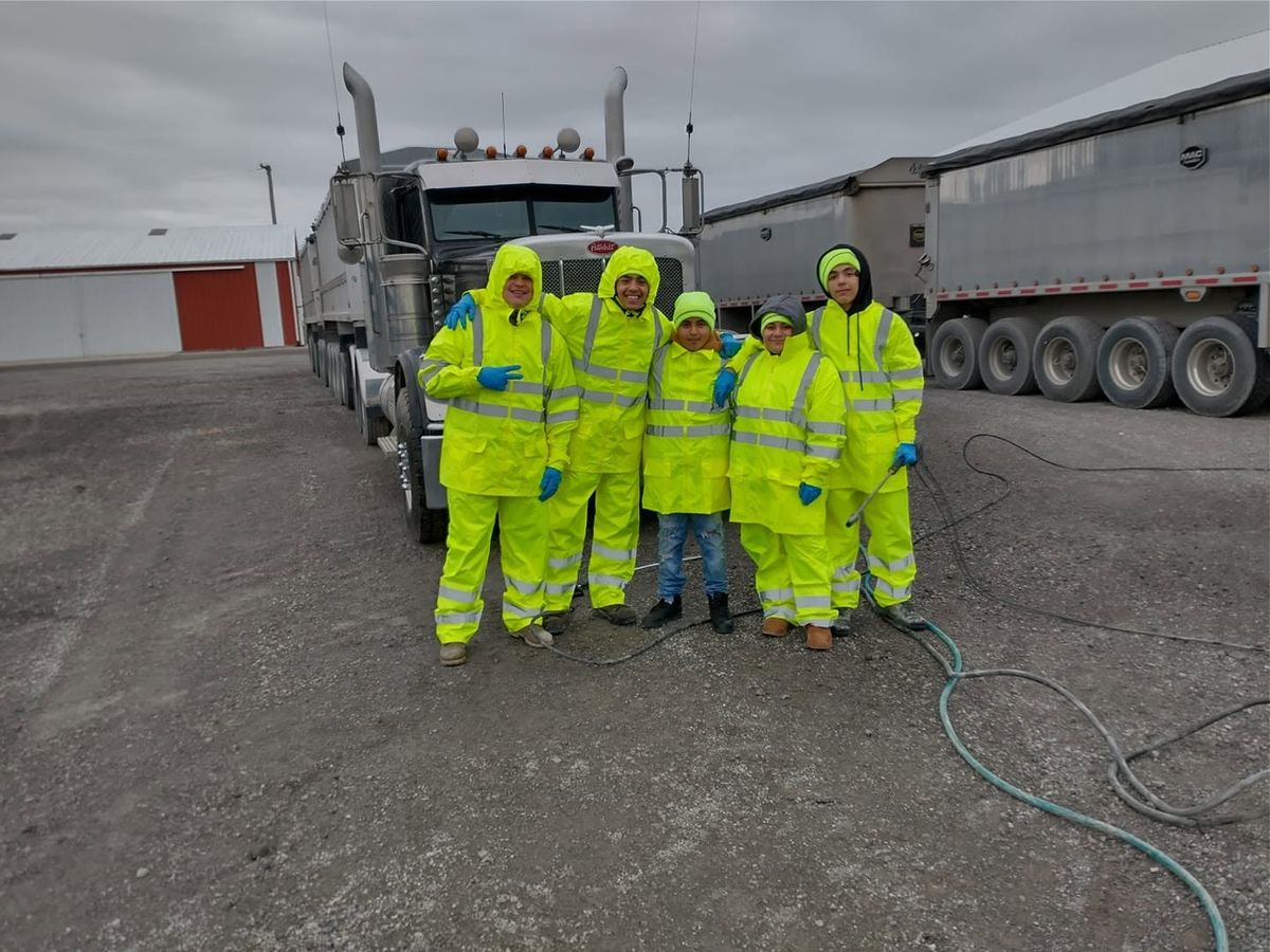 Crew of five in yellow-green rain suits standing arm in arm beside a dump-truck tractor with hoses on the ground.