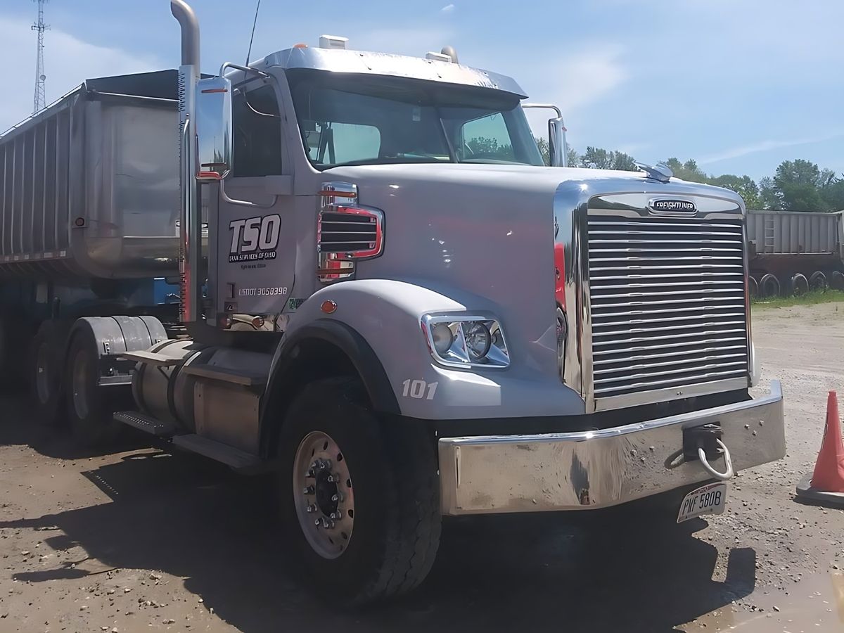 Silver dump-truck tractor with an aluminum dump trailer behind it under a blue sky.