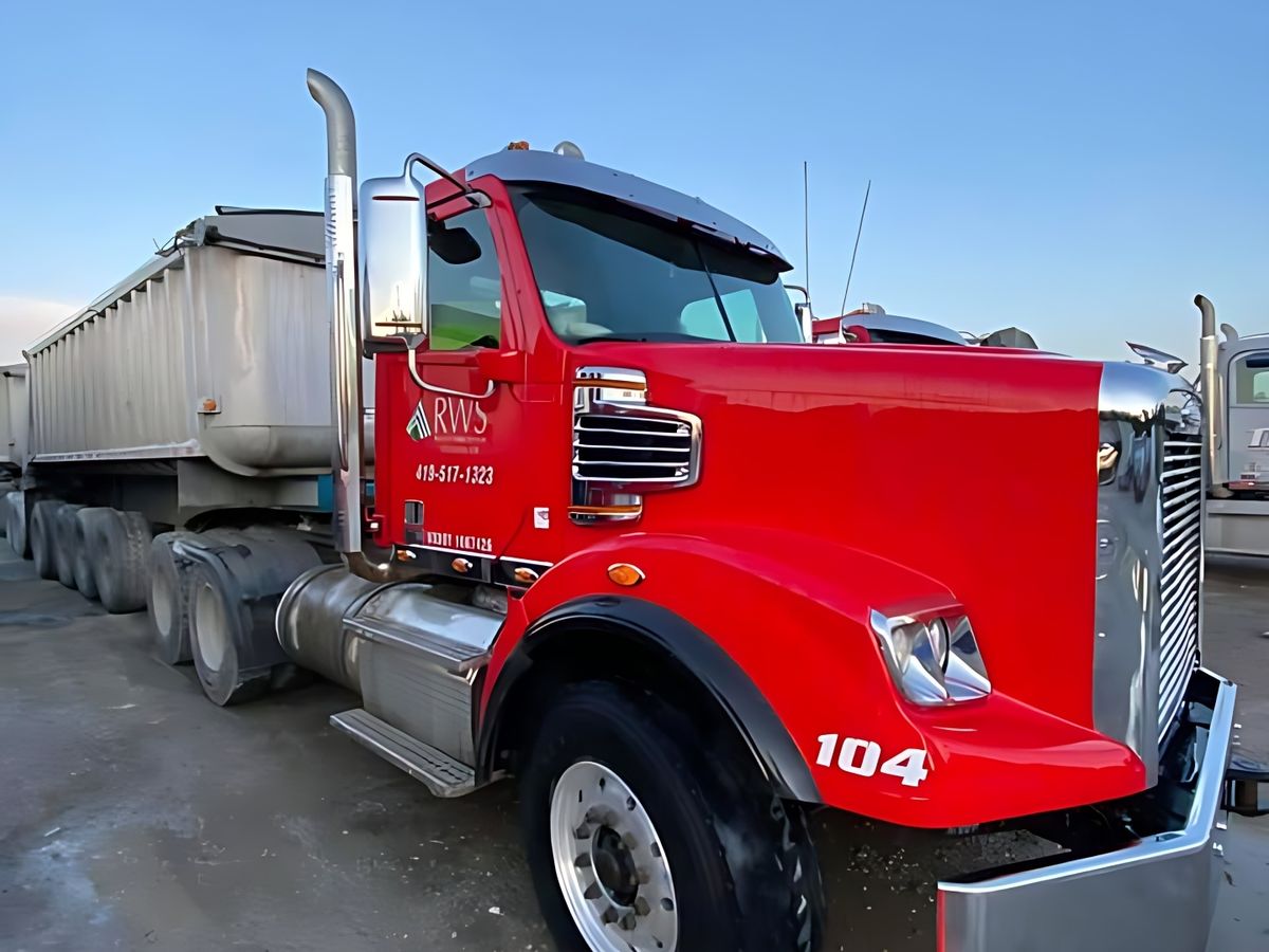 Wet gravel under a red tractor numbered 104 with a chrome bumper and an orange cone.