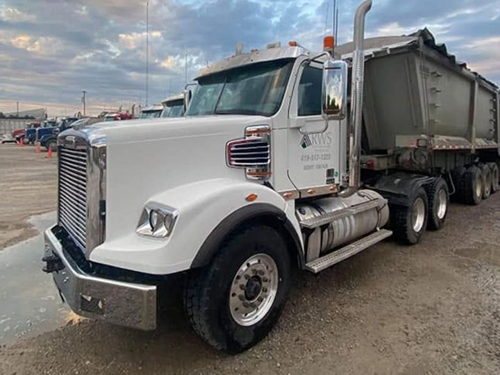 Lower cab, bumper and polished wheel of a white dump-truck tractor, now clean.