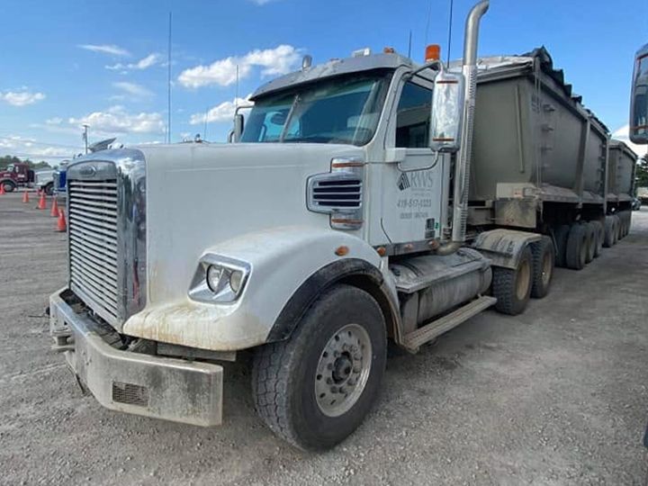 Mud-stained lower cab and bumper of a white dump-truck tractor on a gravel lot.