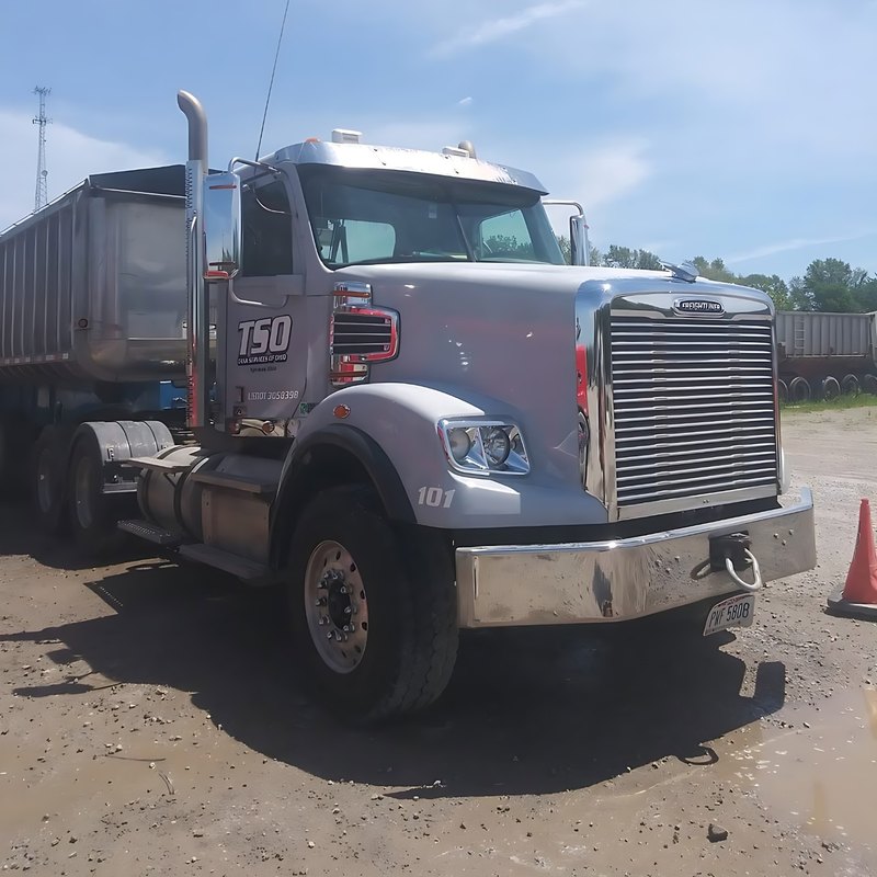 Silver dump-truck cab with a chrome stack and mirror under a blue sky.